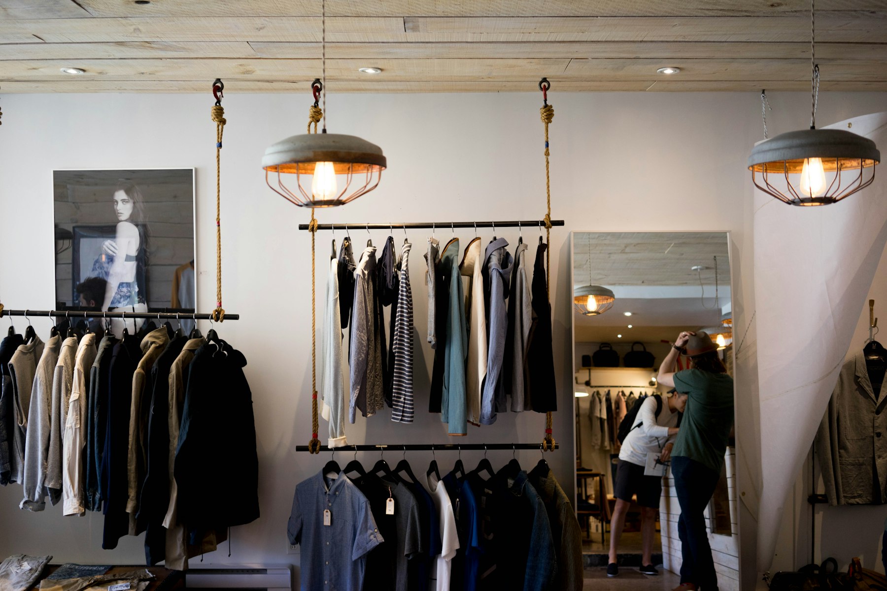 Caged pendant lamps with warm filament bulbs hanging above clothing rails in a boutique